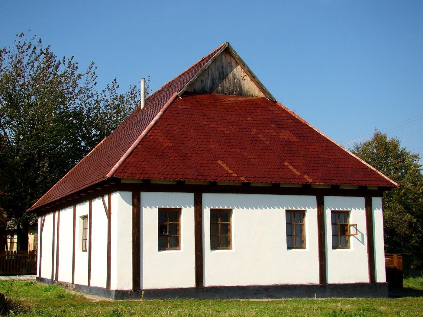 La sinagoga del Baal Shem Tov en Medzhybizh (Podolia, hoy Ucrania), lugar en torno al cual el Besht reunió a su círculo de discípulos hacia 1736. El edificio que se ve hoy —y al que peregrinan los jasidim— no es la estructura original de madera del siglo XVIII: esa fue cerrada por las autoridades soviéticas en 1939 e incendiada en 1942. La construcción actual es una reconstrucción levantada a finales del siglo XX sobre el solar histórico, guiada por fotografías antiguas. Es, por tanto, testimonio del lugar y de su culto continuado, no del aspecto material que conoció el propio Baal Shem Tov.
